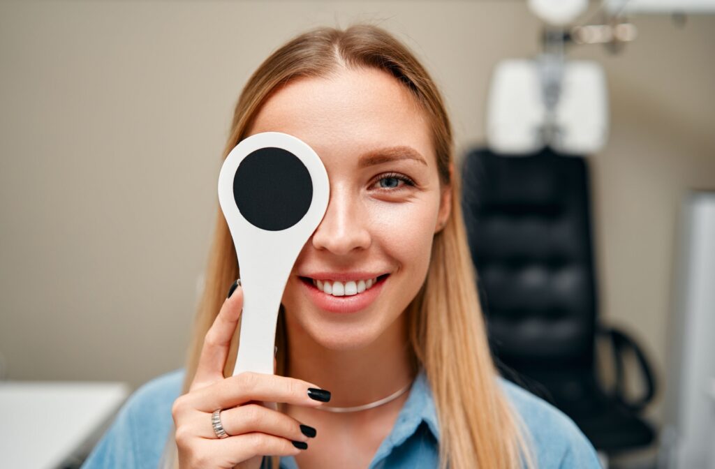A woman in an eye doctor's office holds an eye cover over one eye during an eye exam.