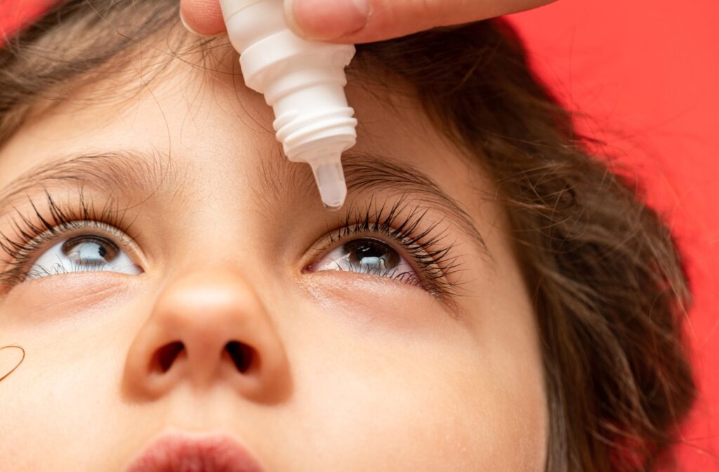 Close-up of a young child's face as their parent assists them with putting eye drops in.