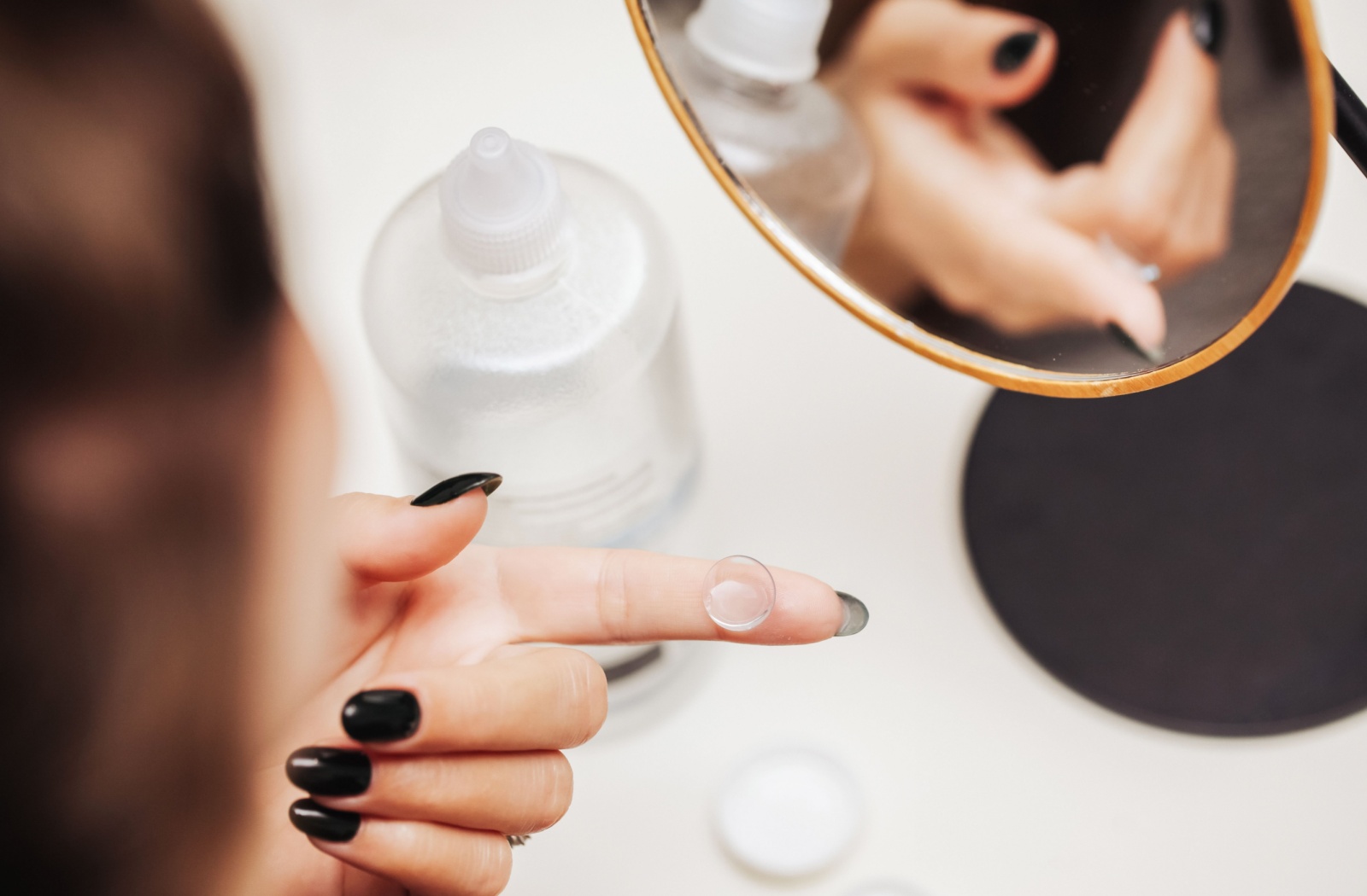 A woman is holding a contact lens to put in her eye for her contact lens fitting.