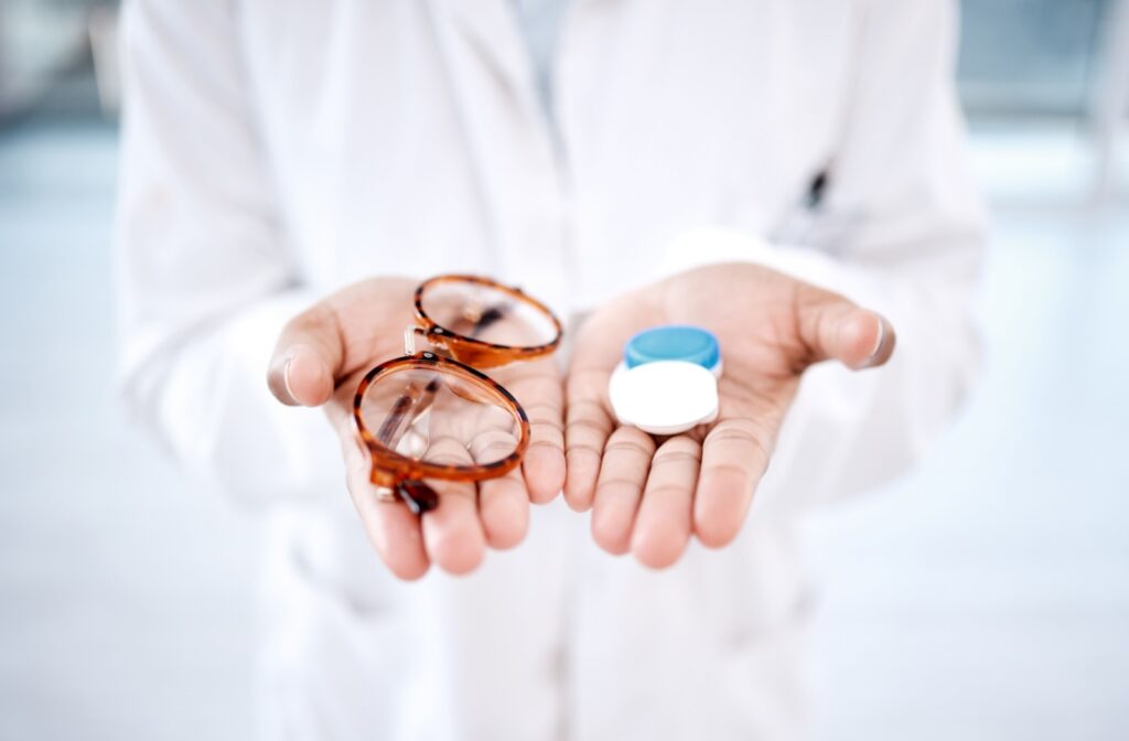 A close-up image of an optometrist holding out a pair of eyeglasses and contact lenses to explain the difference in prescriptions.