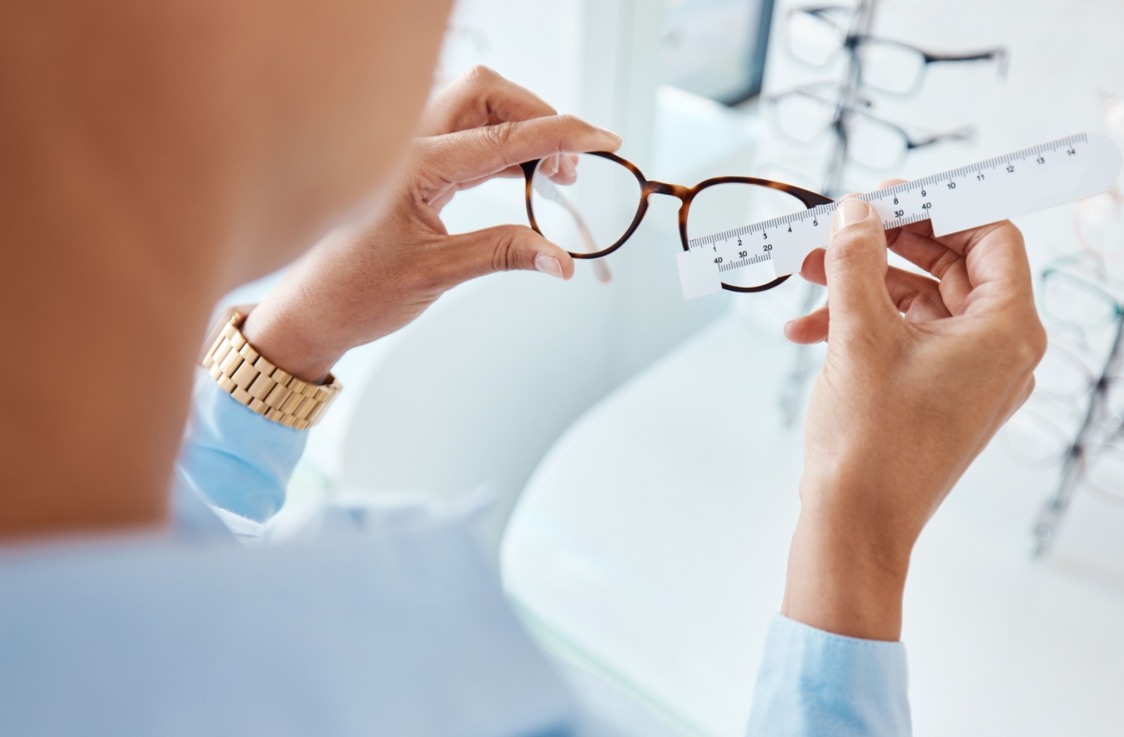 An optometrist uses an optic ruler tool to measure and prepare a pair of eyeglasses for a patient