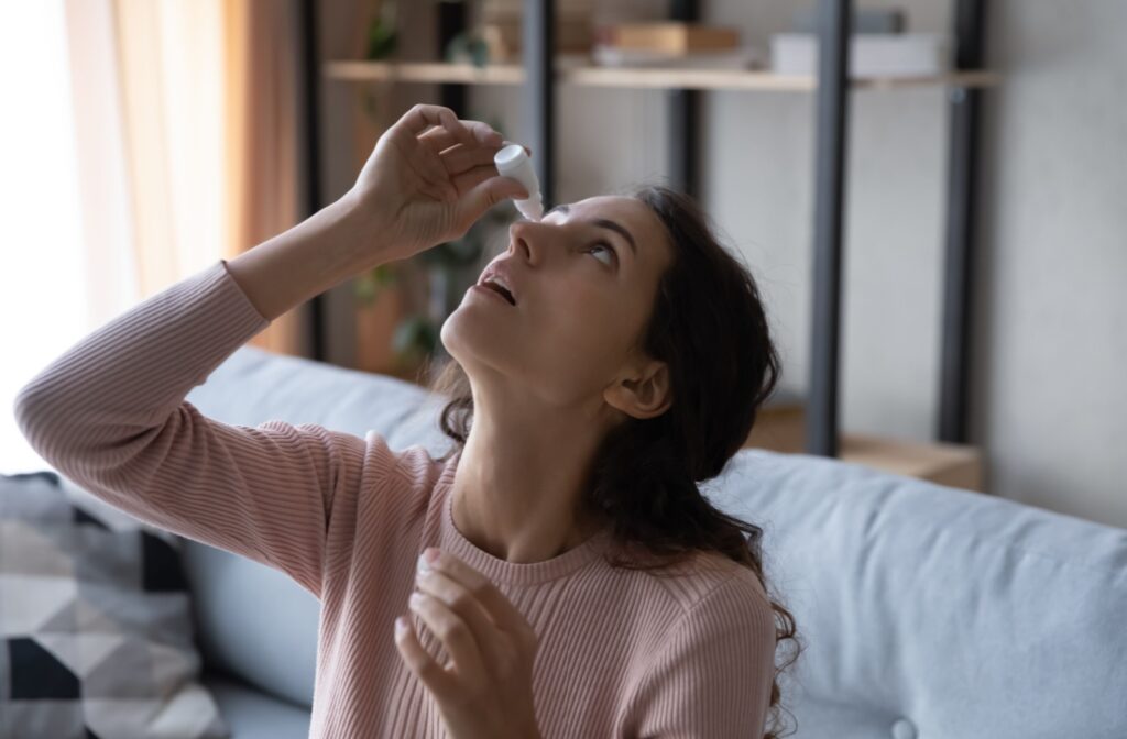 A young woman applying artificial tears to her dry eyes.