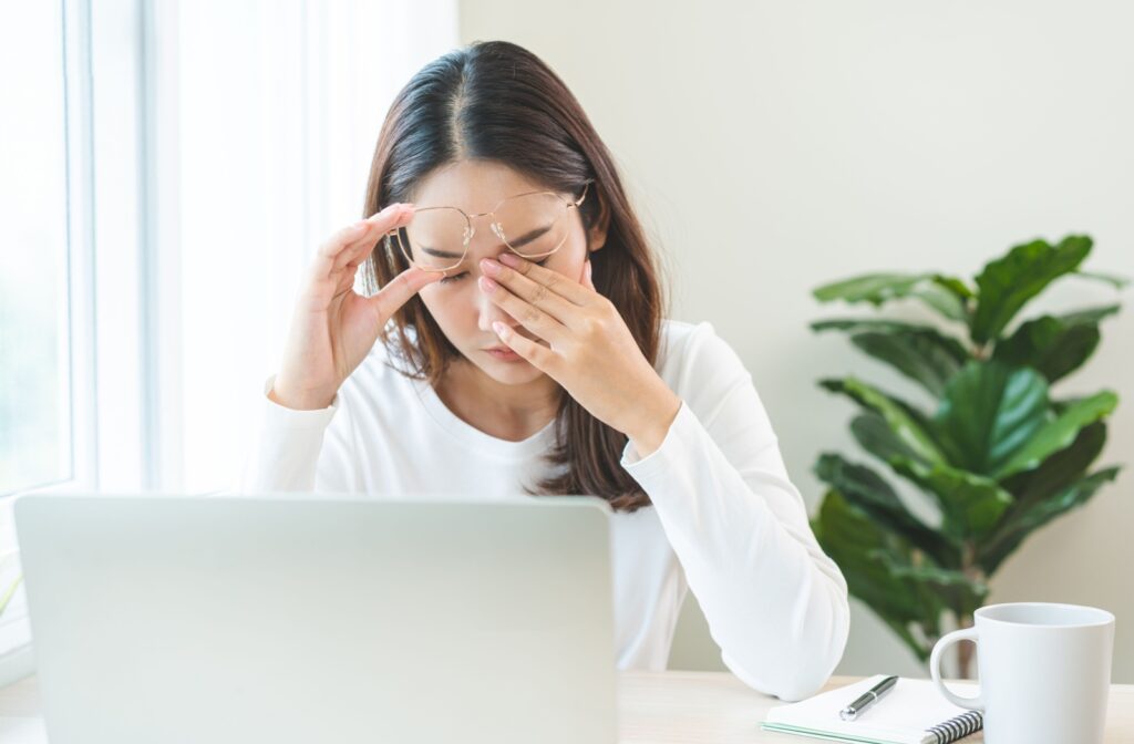A person rubbing their eyes due to blurry vision from dry eyes while working at a computer.