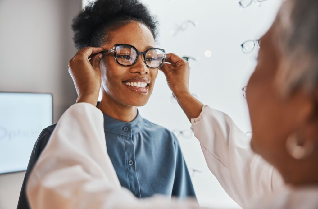 Optician placing glasses on a smiling patient during a fitting.