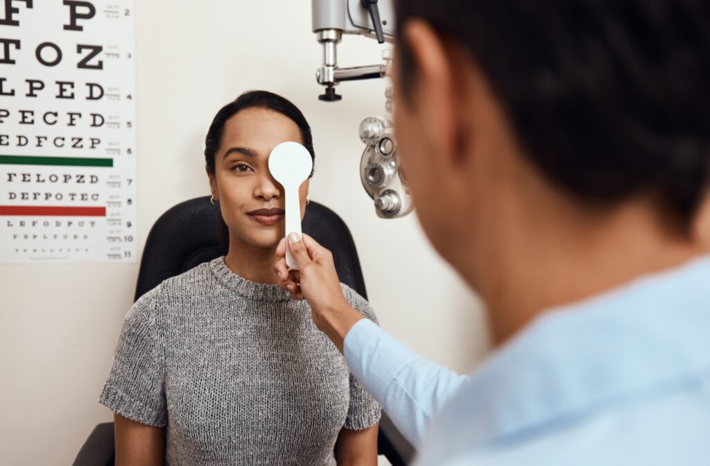 A person sits in an exam chair as an optometrist holds a vision occluder over one of her eyes during a routine eye exam.