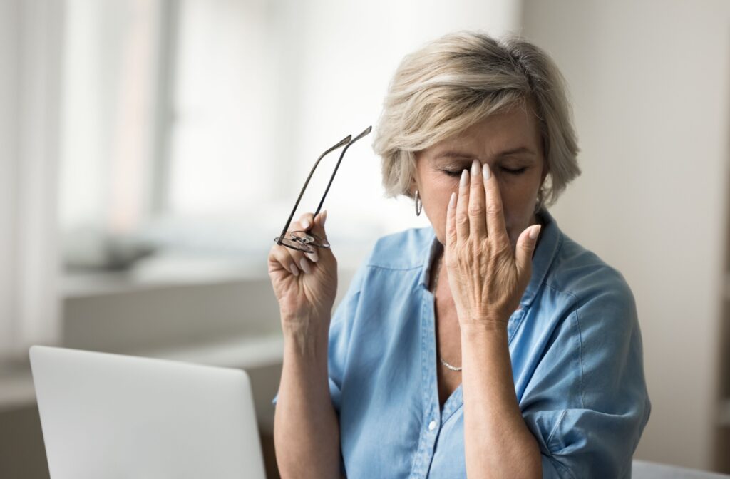 A person holds their glasses away from their face while their other hands soothes their eye