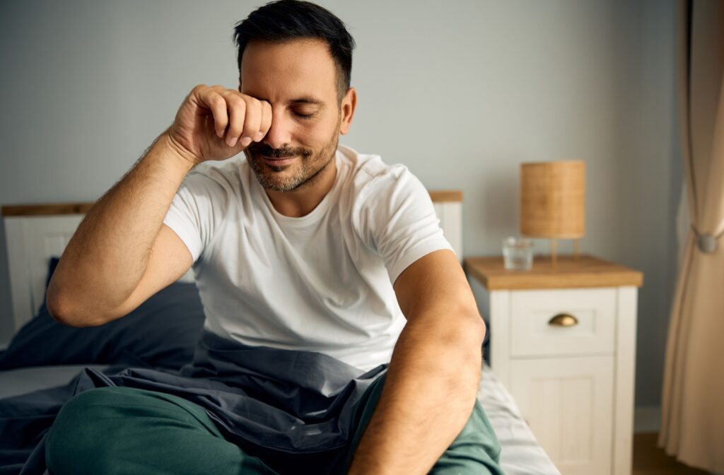 A person sitting up in bed after waking up rubbing their dry eyes